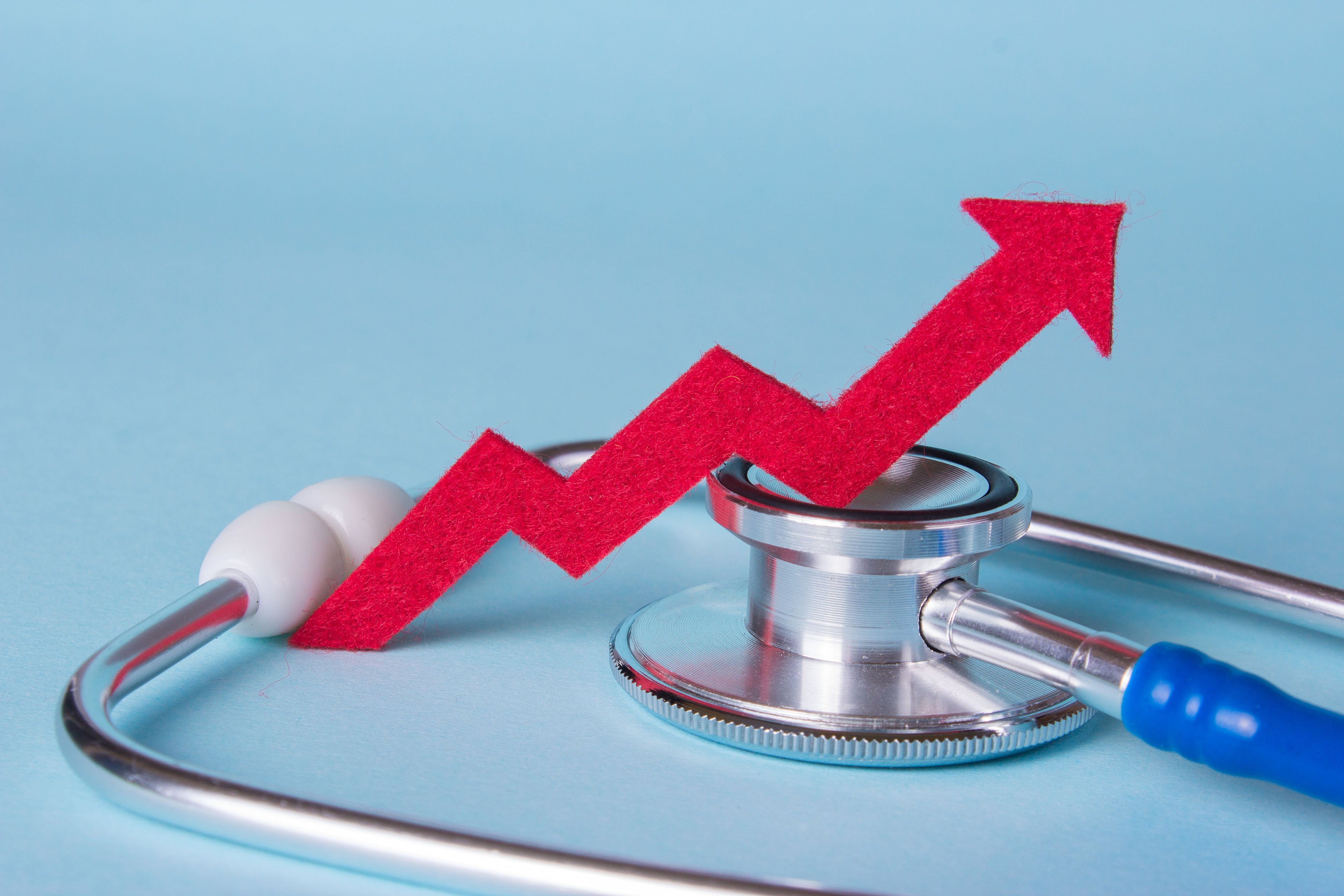 An upward red arrow rests on a stethoscope on a pale blue background.
