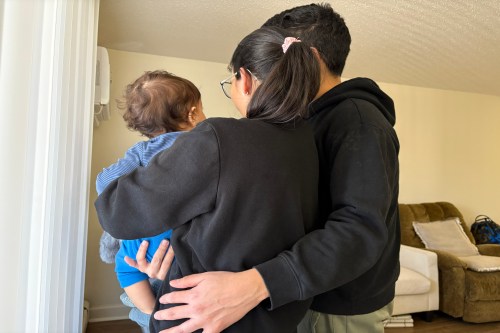 The back of a mother, father, and young baby being held by its mother. They are embracing.