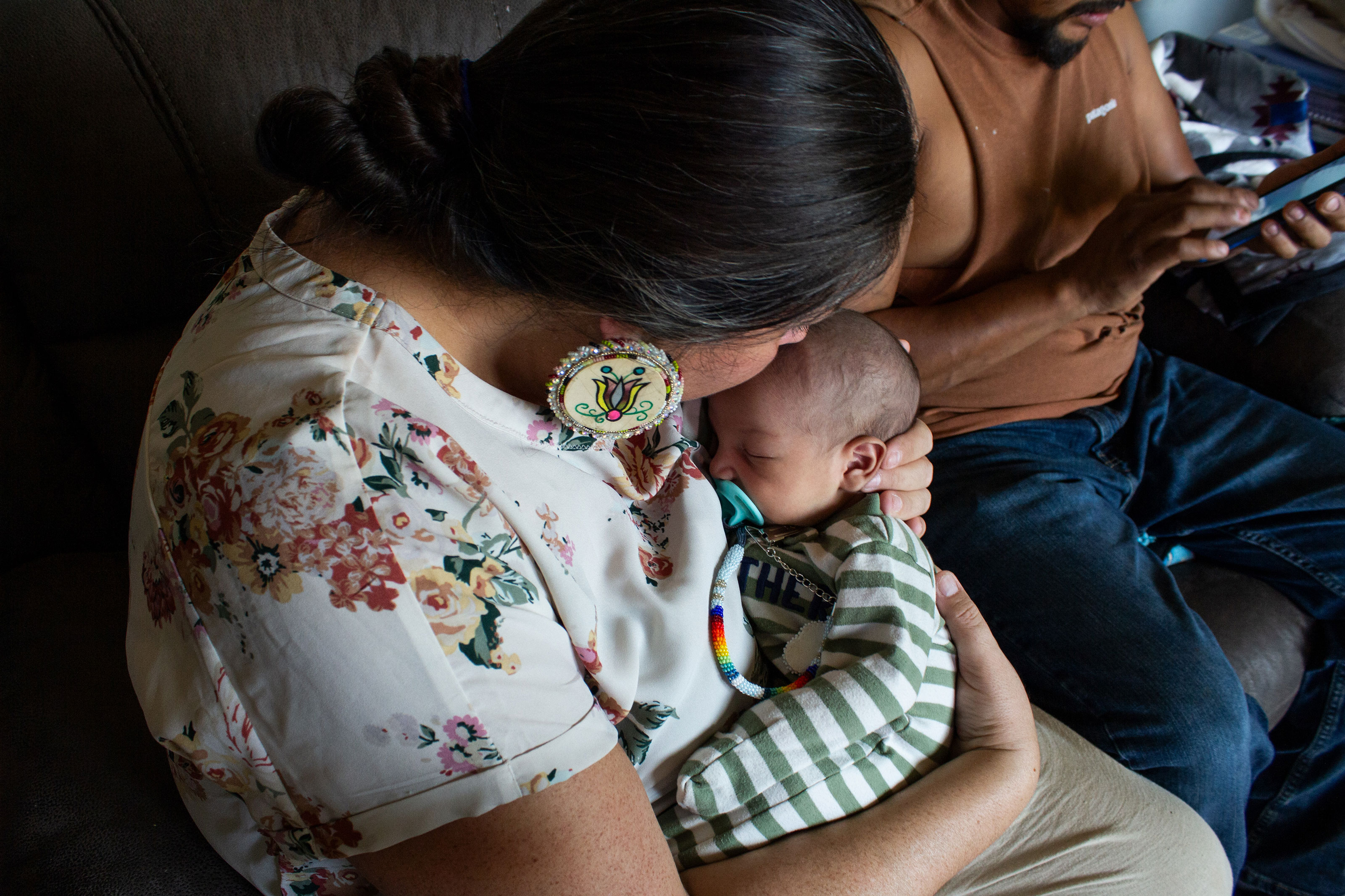 A doula holds a baby while sitting on a couch.